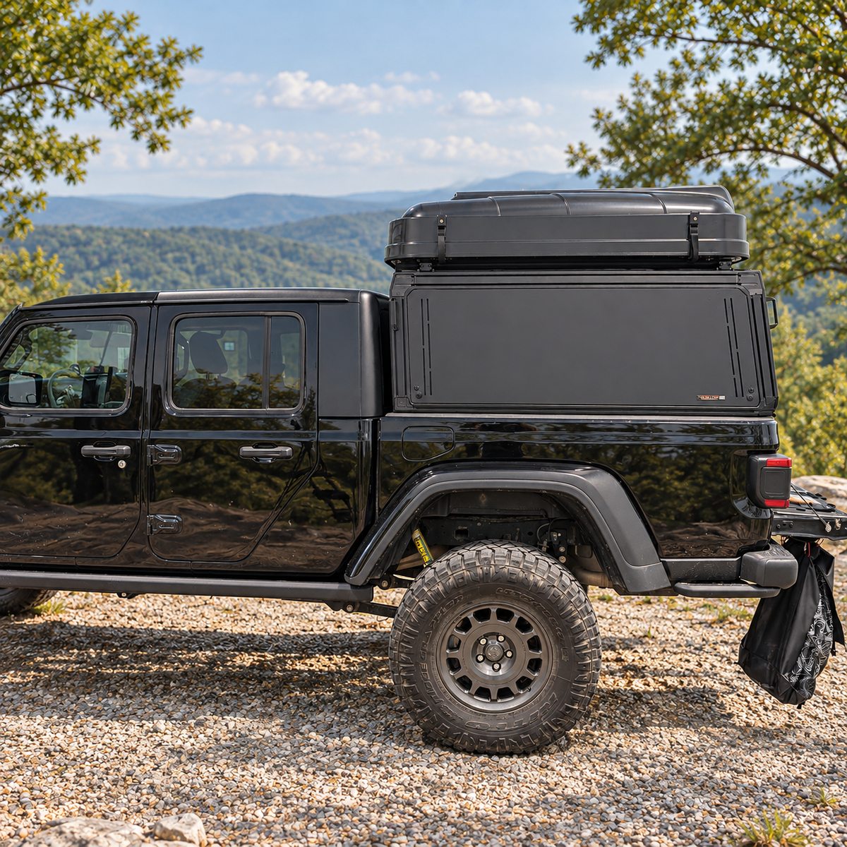 Black Jeep Gladiator with XO.SKLTN truck cap topper, side view at a wooded overlook