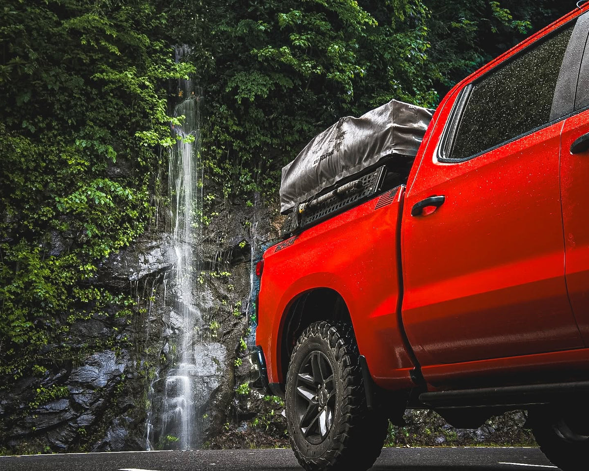Rooftop tent on XBRS bed bars on a red Silverado parked by a waterfall