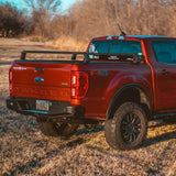 Red Ford Ranger with XBRS truck bed cross bars, rear three-quarter view on dry grass